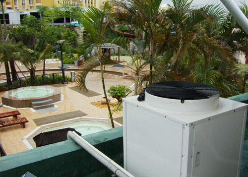 Aufsicht von einem Hausdach auf eine Poolanlage, eine Wärmepumpe rechts fokussiert im Bild für die Poolheizung