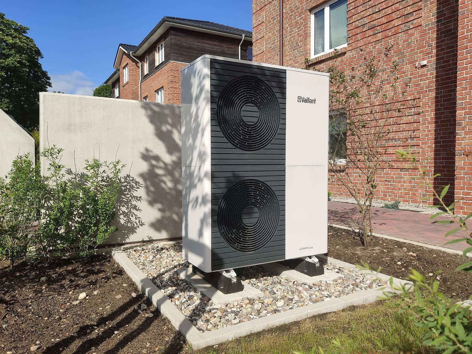 Bild einer Luft-Wasser-Wärmepumpe von Vaillant neben einer Außenhauswand im Sonnenschein